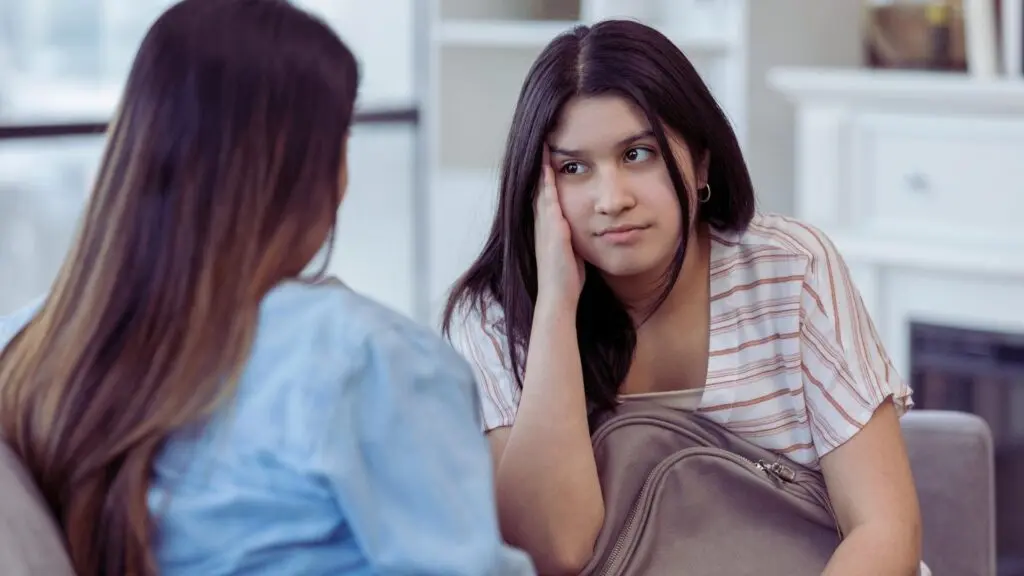 Teen looking stressed while talking with a parent about concerning behavior.