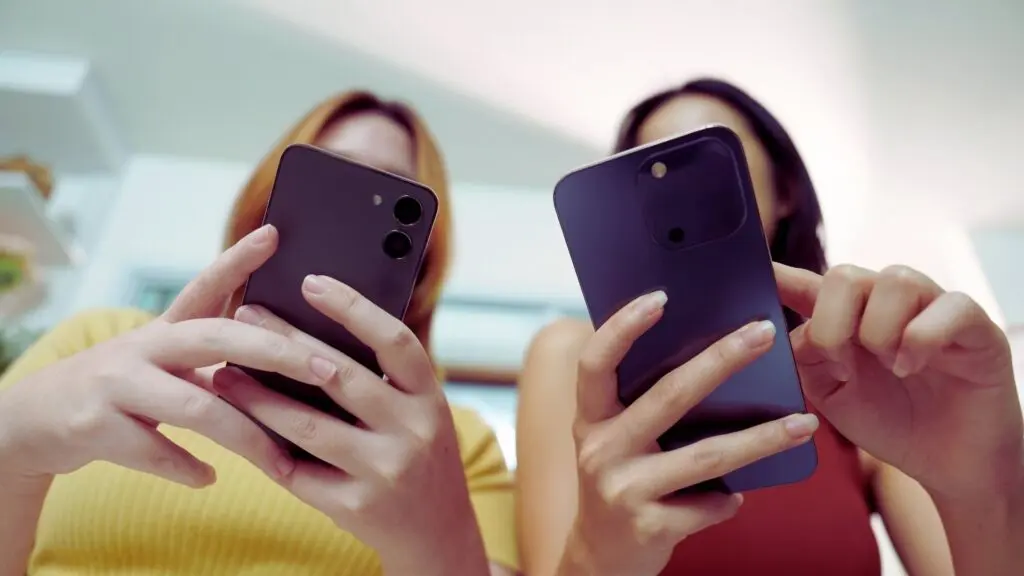 Two teens using smartphones together, representing online influence and peer behavior