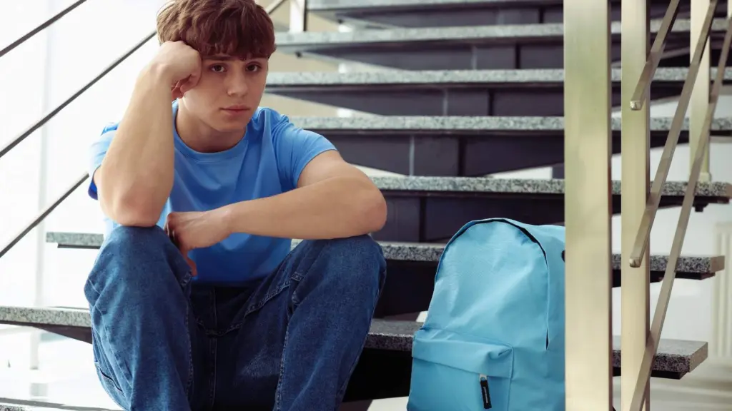 Teen sitting alone on school stairs with backpack, appearing withdrawn